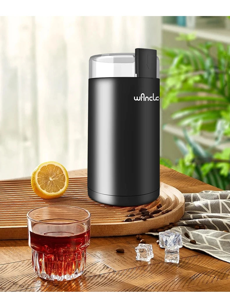 Moulin à café électrique noir sur une table en bois à côté d'un verre de thé