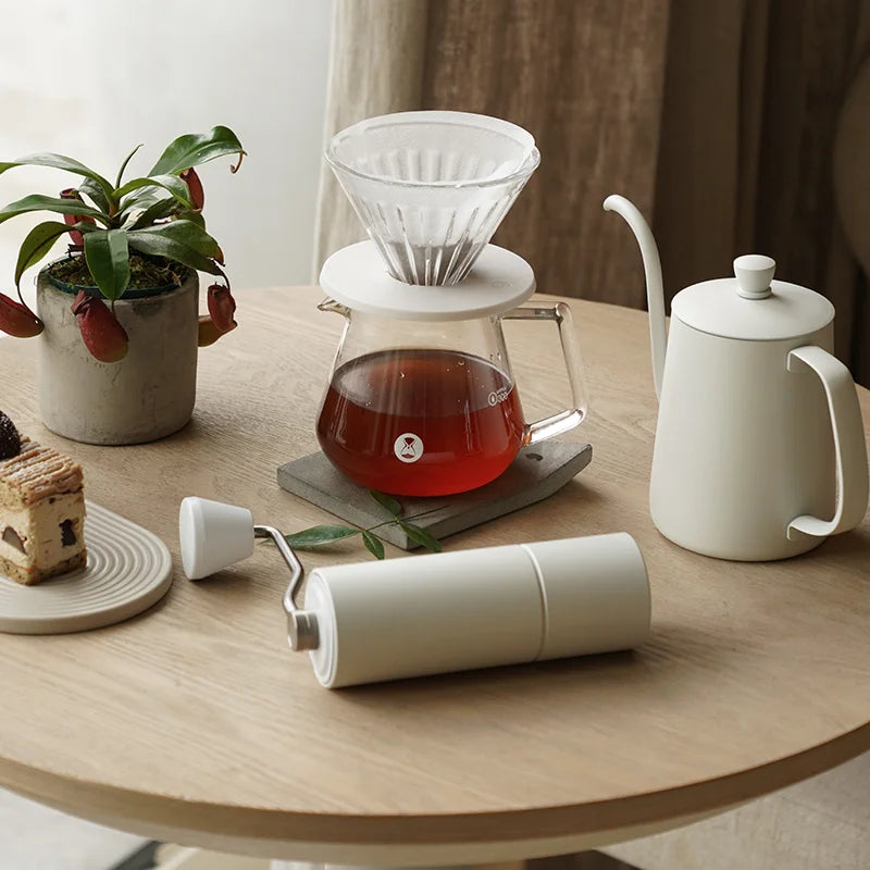Moulin à café manuel blanc sur une table à côté d'une carafe de café filtre